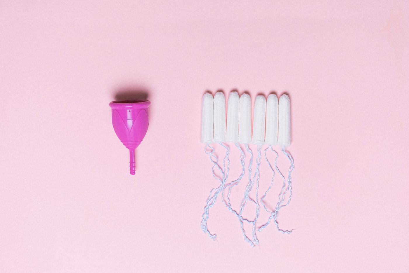 Cupa menstruala si tampoane pe fundal roz